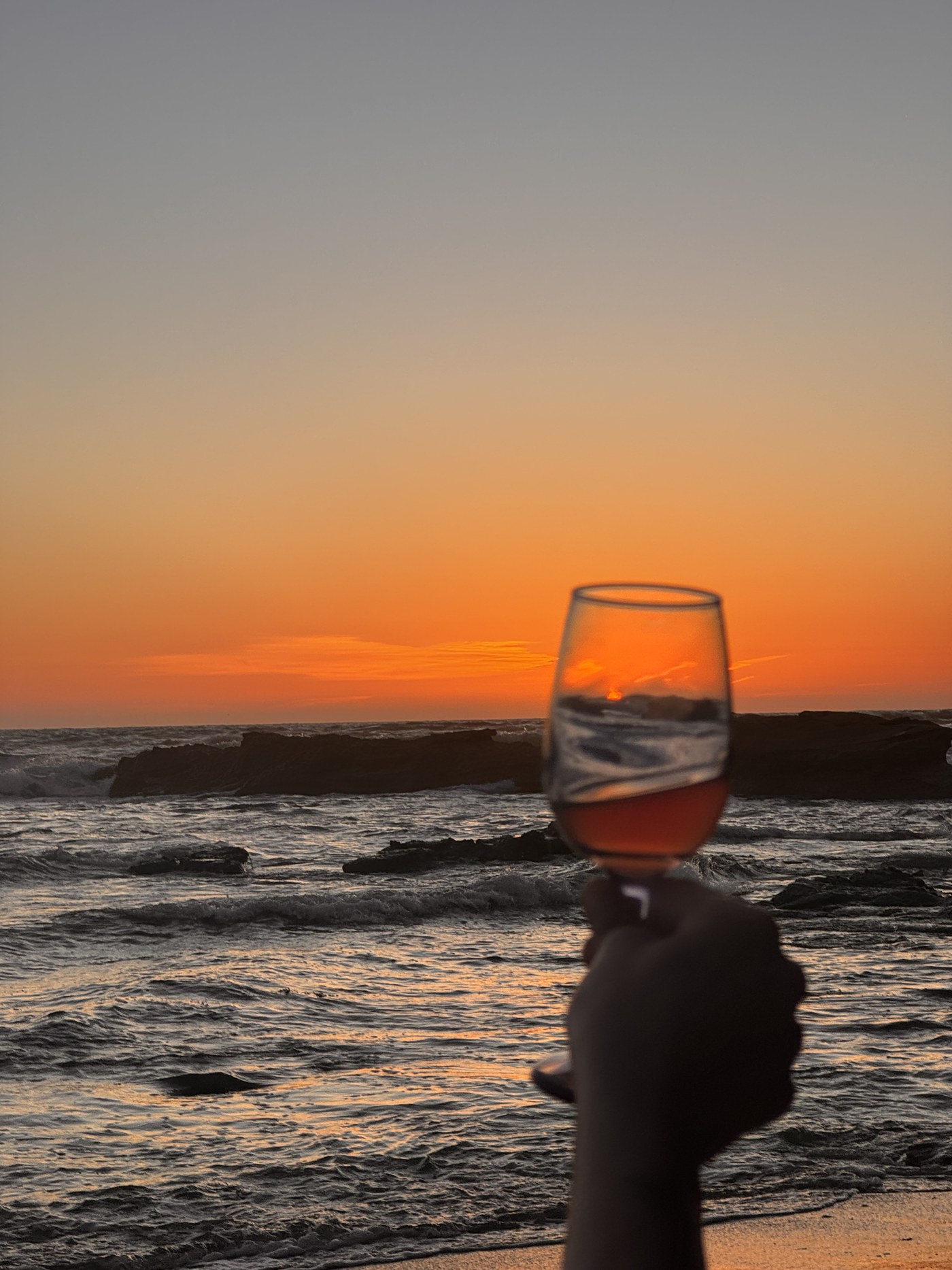 A glass of wine raised against an ocean sunset